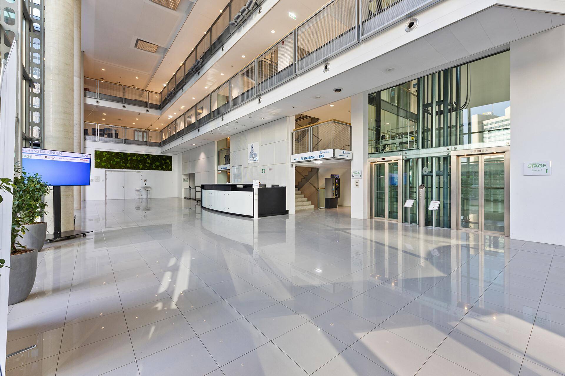 Geräumige, moderne Lobby mit glänzendem Fliesenboden, Rezeption und sichtbaren Aufzügen.
