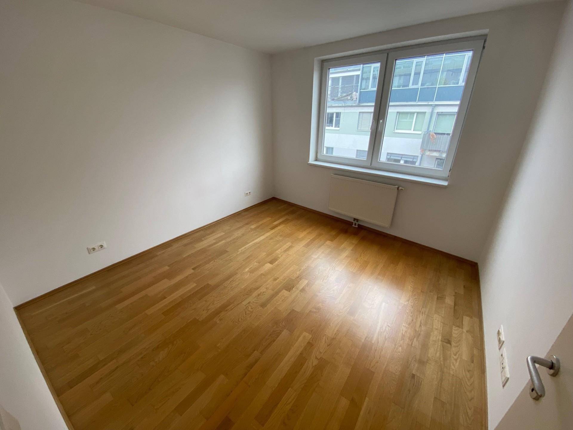 Weiteres Schlafzimmer mit Parkettboden und großem Fenster.