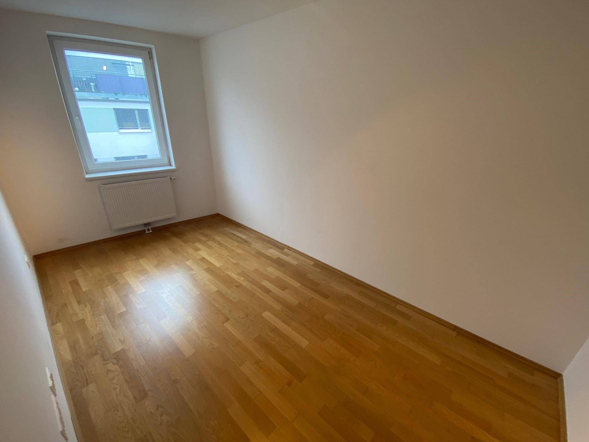 Schlafzimmer mit Parkettboden und Fenster, das viel Tageslicht hereinlässt.