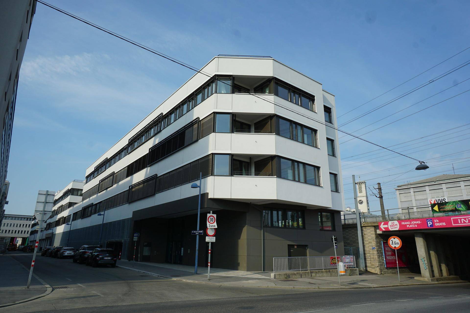 Modernes Bürogebäude mit weißer Fassade und dunklen Fensterrahmen an einer städtischen Straße.