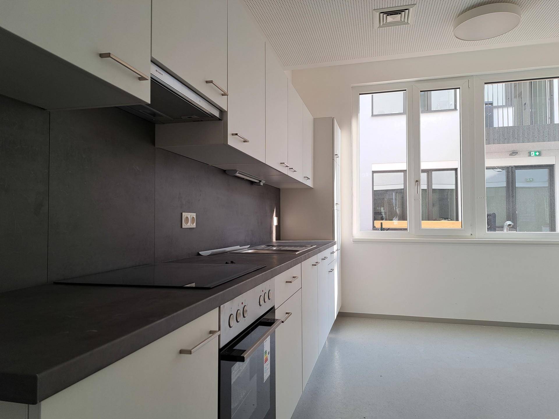 Moderne Einbauküche mit weißen Schränken, dunkler Arbeitsplatte und Fensterblick.