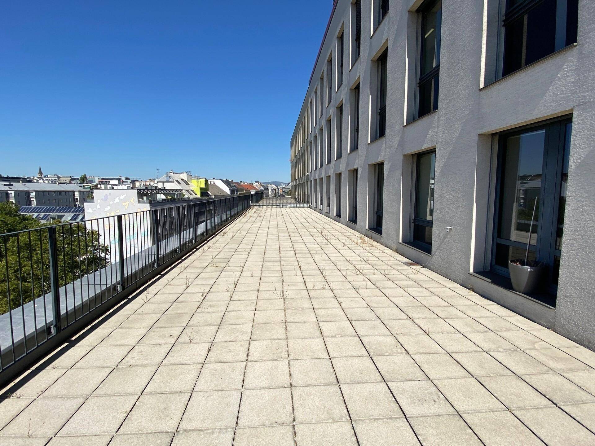Weitläufige Dachterrasse mit Fliesenboden und Blick auf die umliegende Stadtlandschaft.