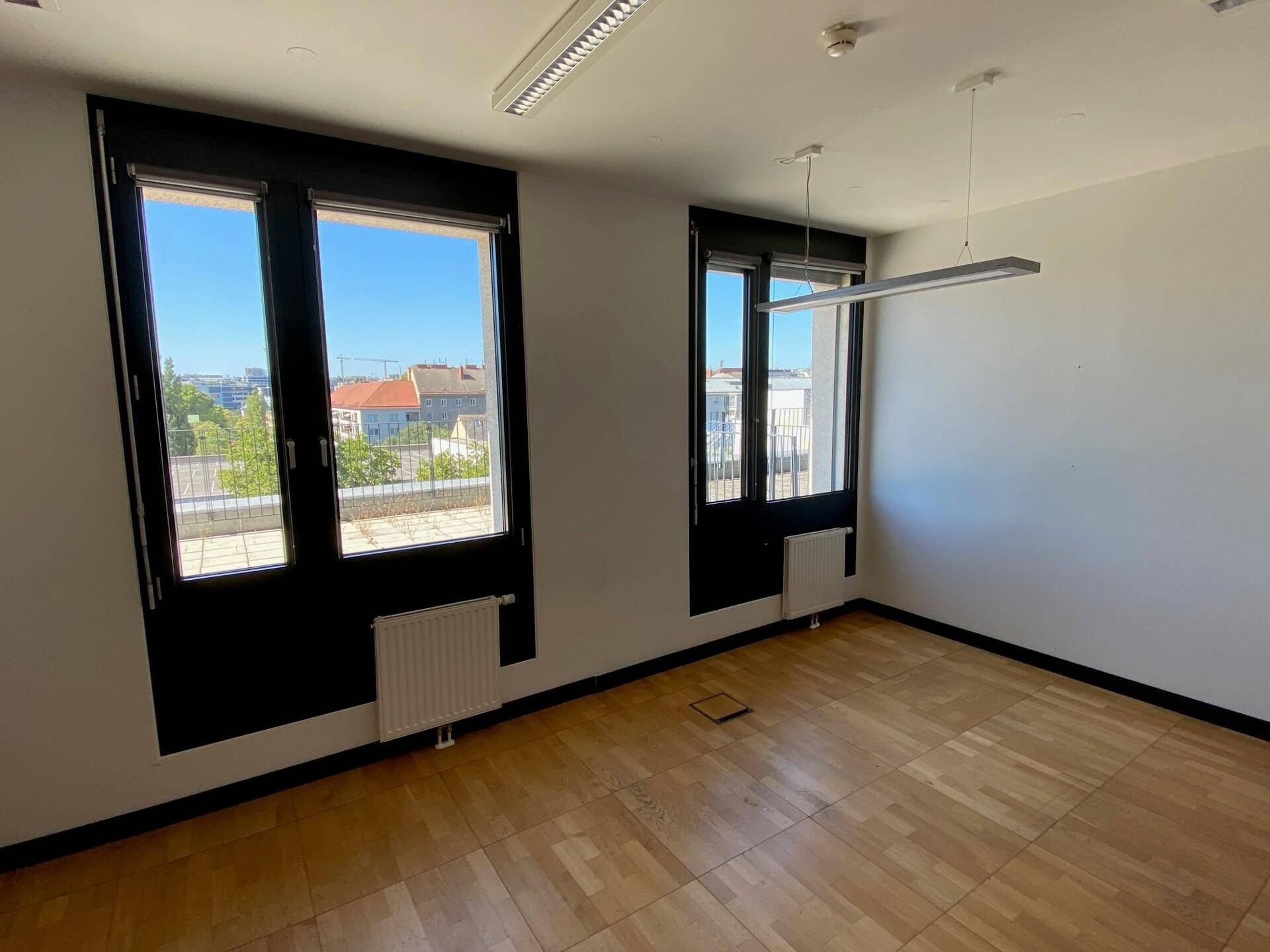 Geräumiger Büroraum mit Parkettboden und Fenstern, die einen weiten Blick über die Stadt ermöglichen.