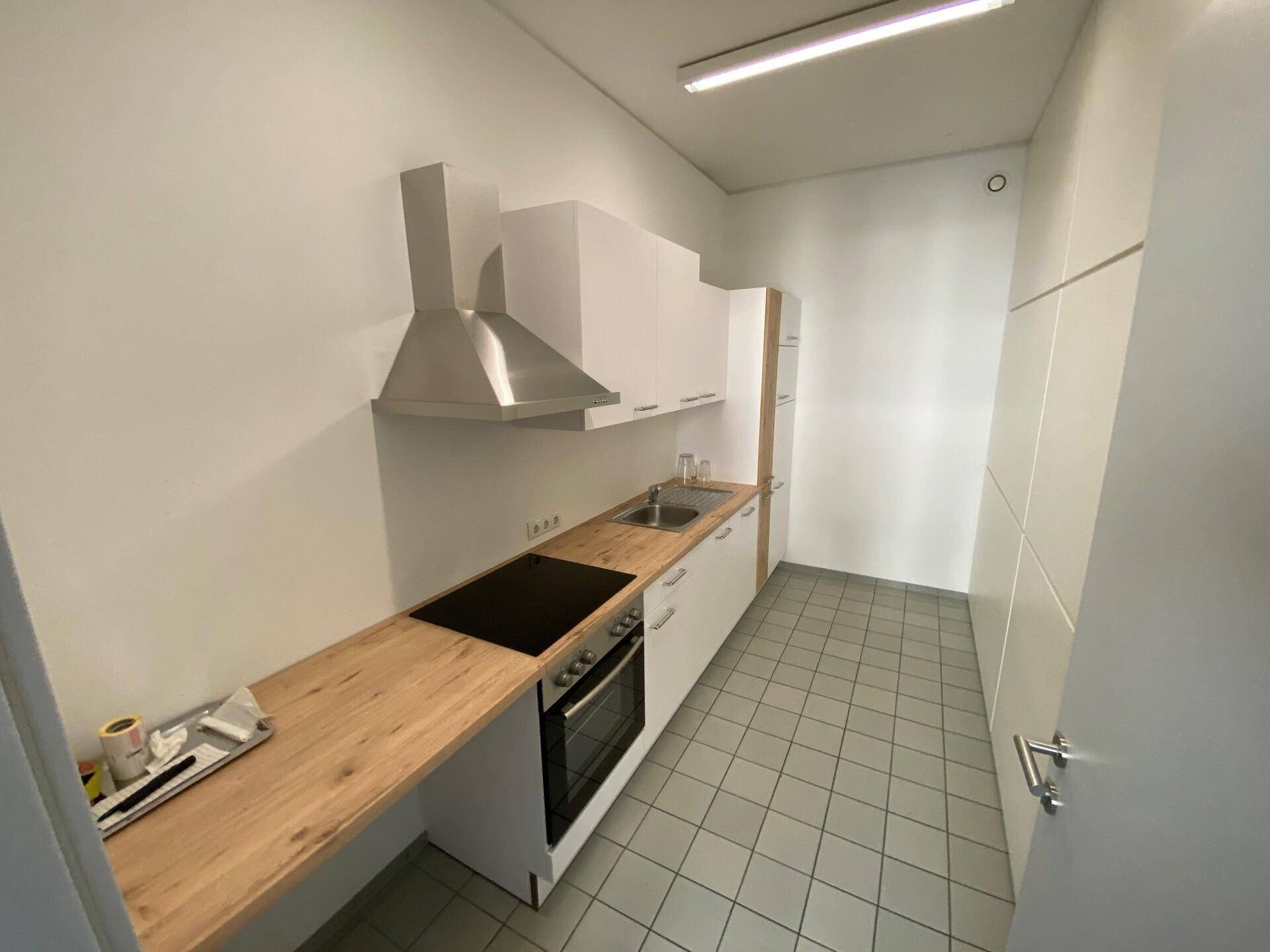 Moderne Einbauküche mit weißen Schränken, Holzarbeitsplatte und Edelstahl-Dunstabzugshaube.