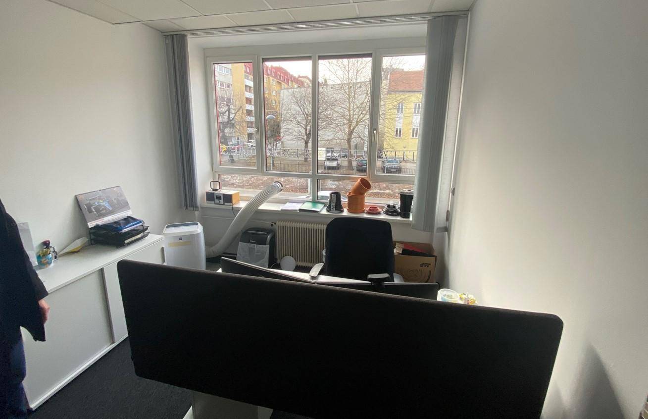 Möblierter Büroraum mit Schreibtisch, Stuhl und Stauraum, bietet Blick auf die umliegende Straße.