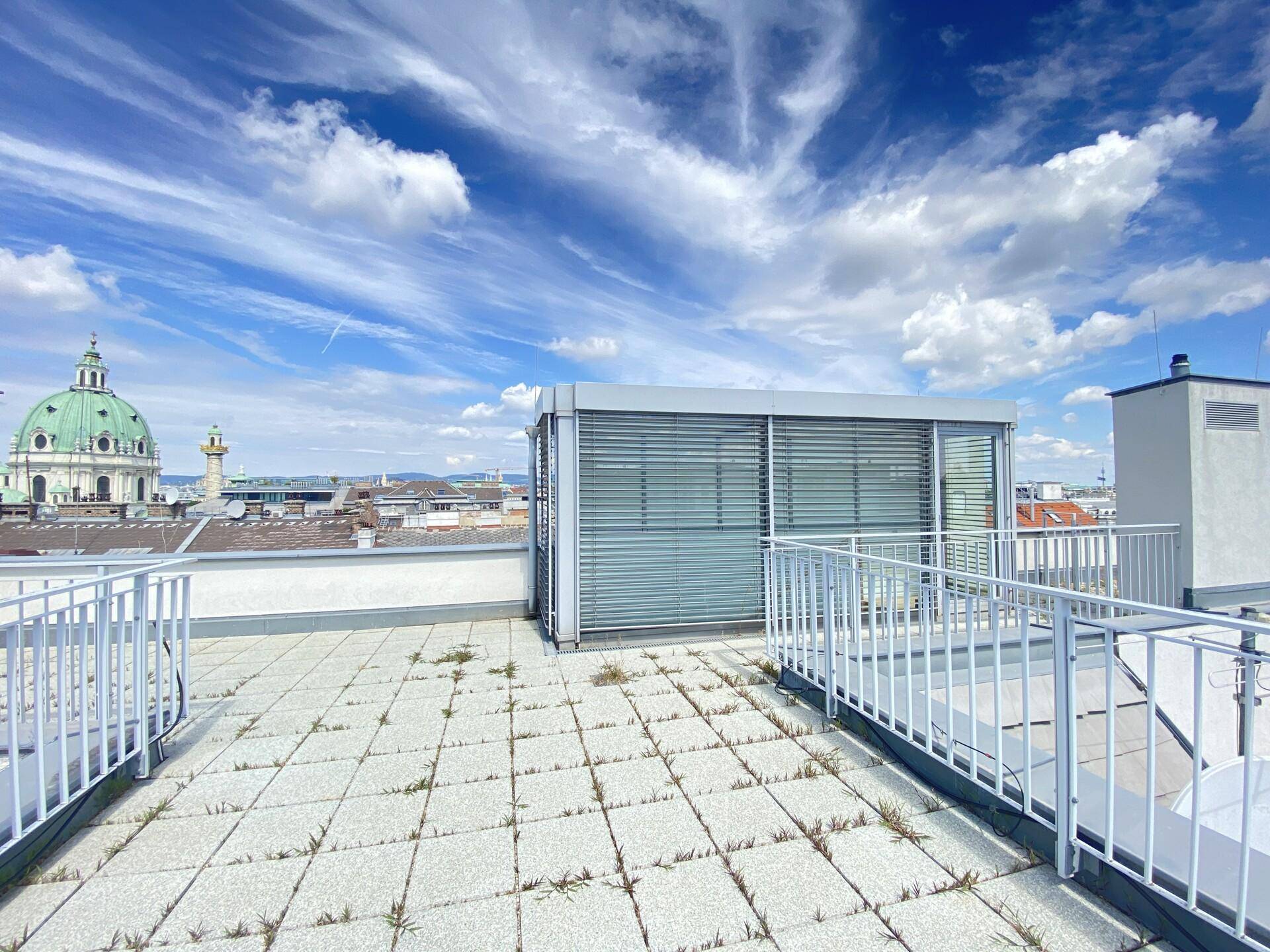 Geräumige Dachterrasse mit Fliesenboden und Blick auf die Wiener Skyline.