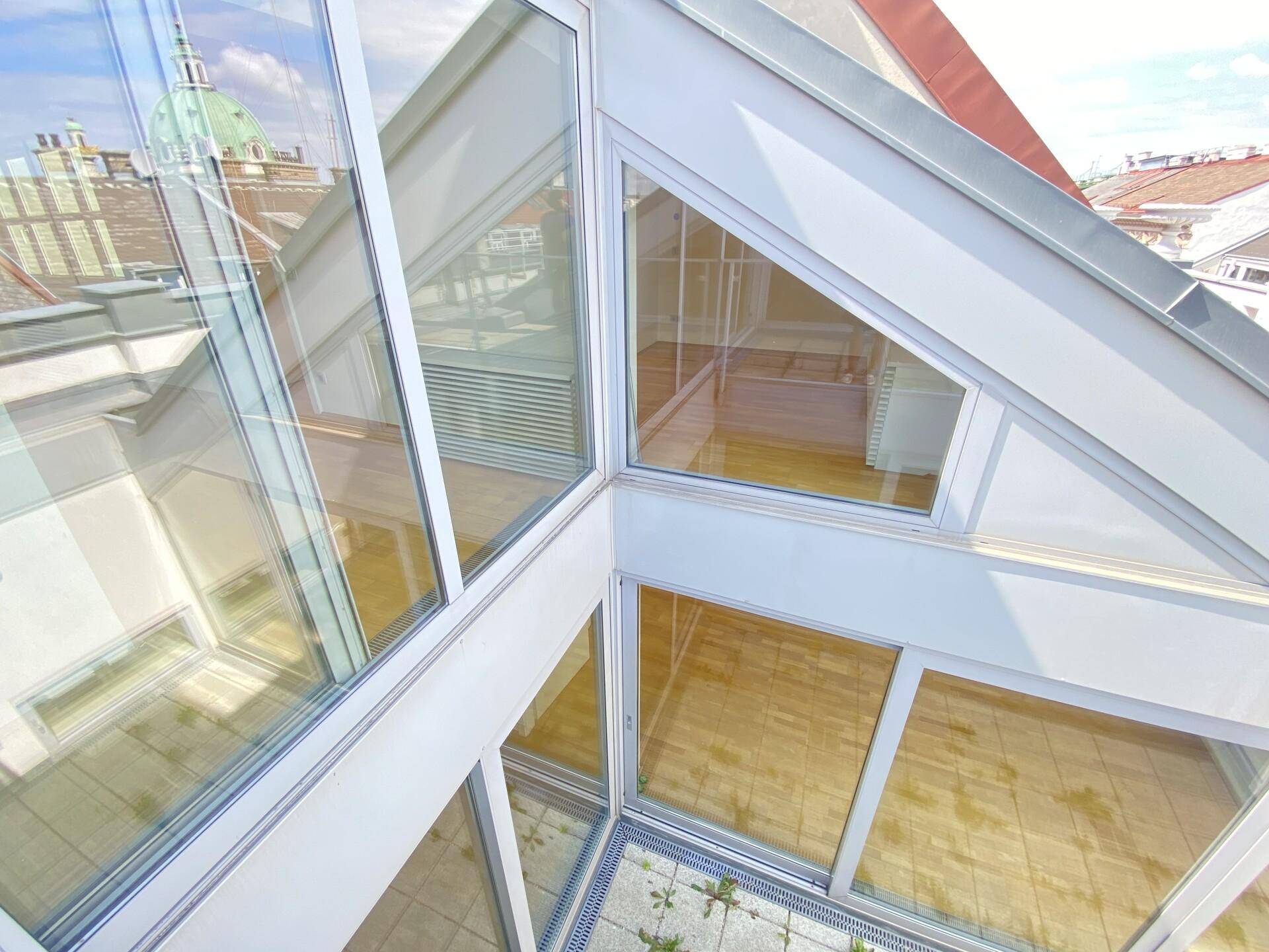 Moderne Glasarchitektur mit schrägen Fenstern und Blick auf die Stadt.