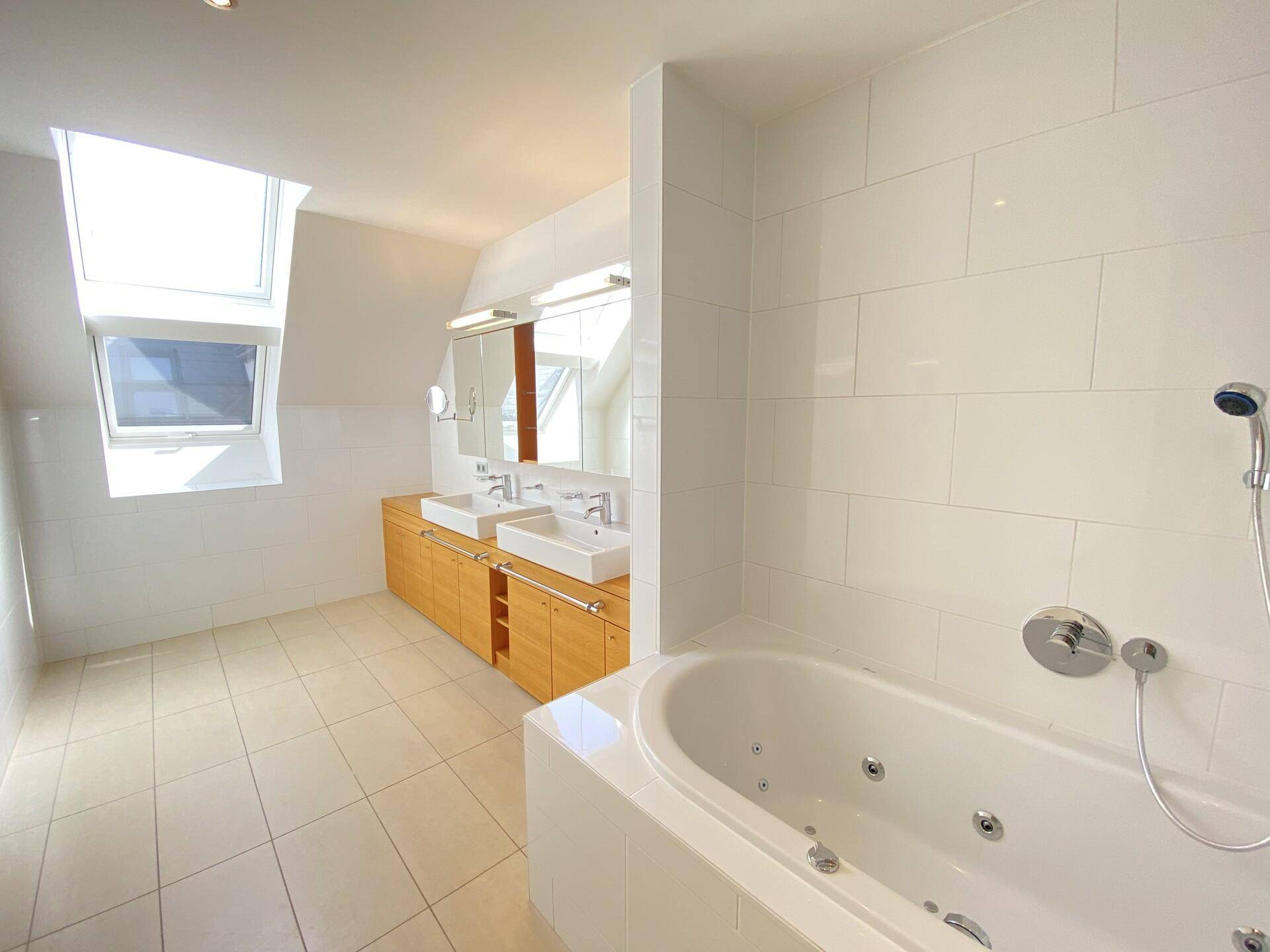 Modernes Badezimmer mit Badewanne, Doppelwaschbecken und Oberlicht für natürliches Licht.