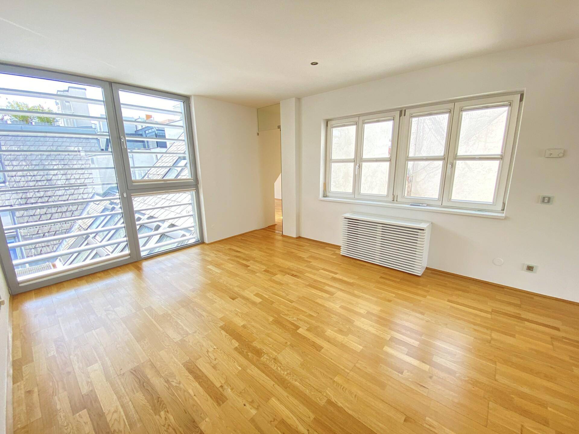 Geräumiger Raum mit Holzparkett und großen Fenstern, bietet viel Helligkeit.