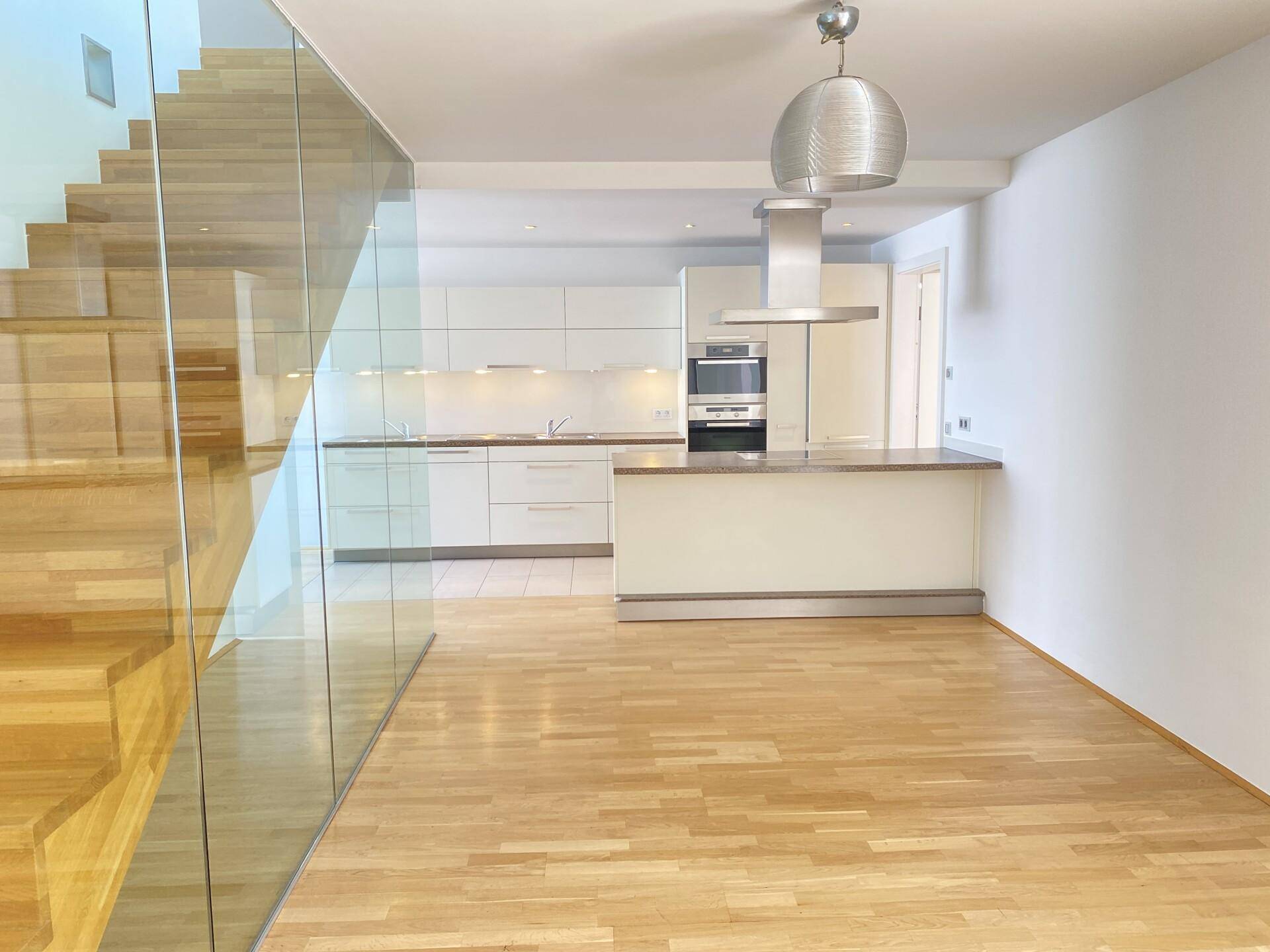 Moderne Einbauküche mit Kochinsel, Dunstabzugshaube und hellem Holzfußboden in offenem Wohnbereich.