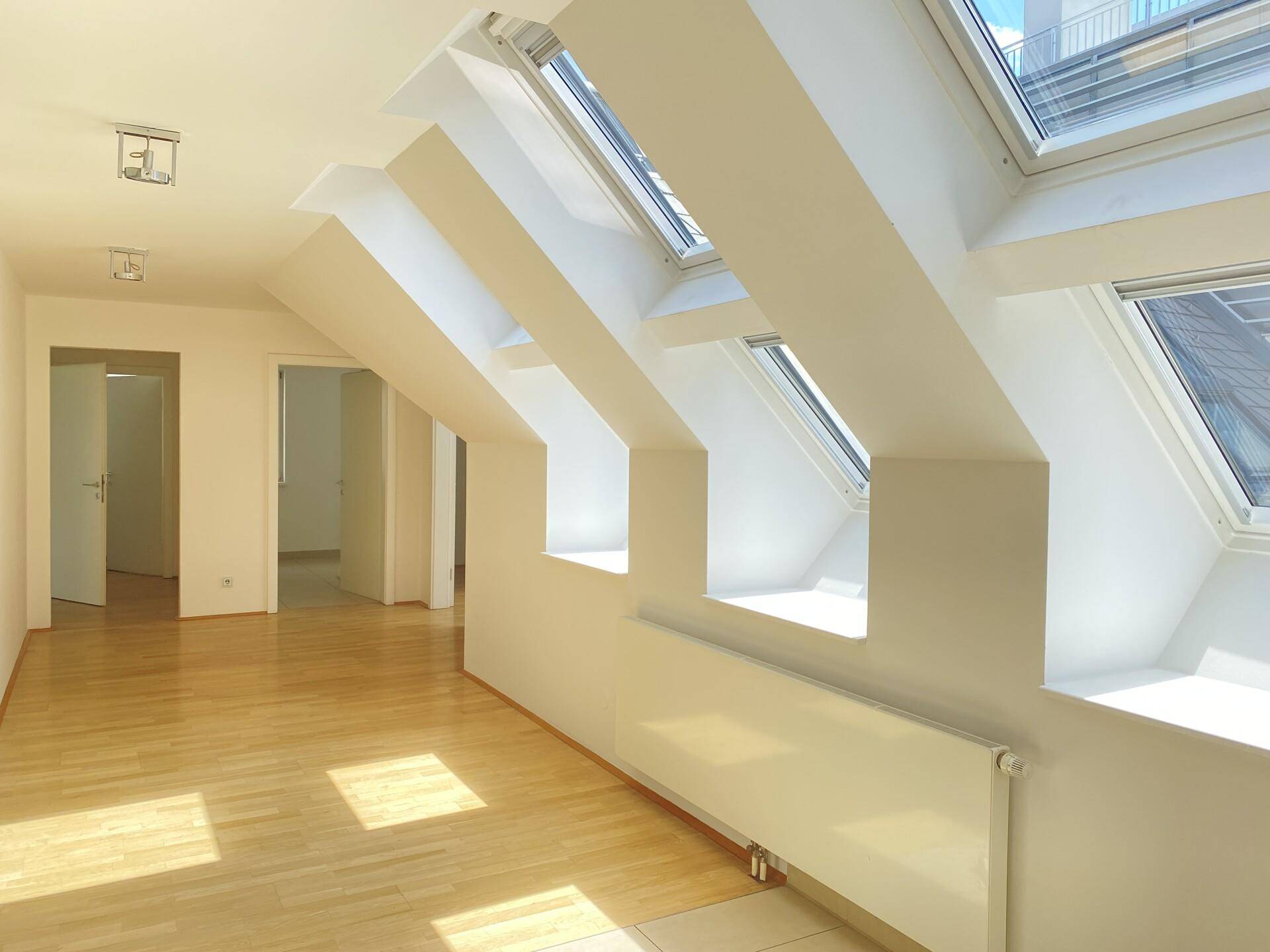 Lichtdurchfluteter Dachgeschossraum mit mehreren Dachfenstern und hellem Holzfußboden.