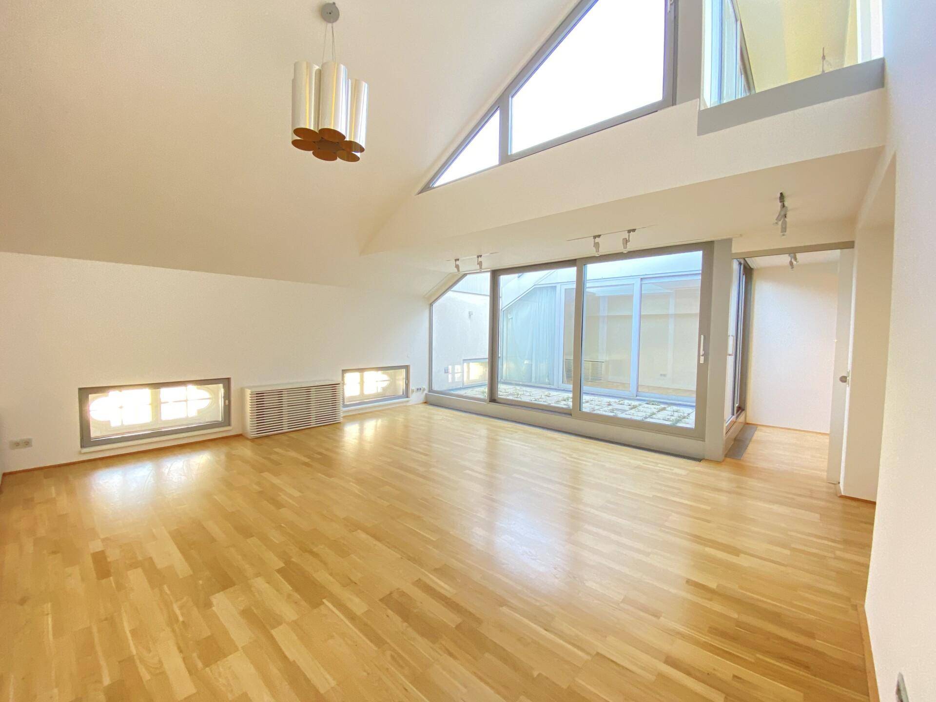 Geräumiges Wohnzimmer mit hohen Decken, großen Fenstern und Zugang zu einem Innenhof.
