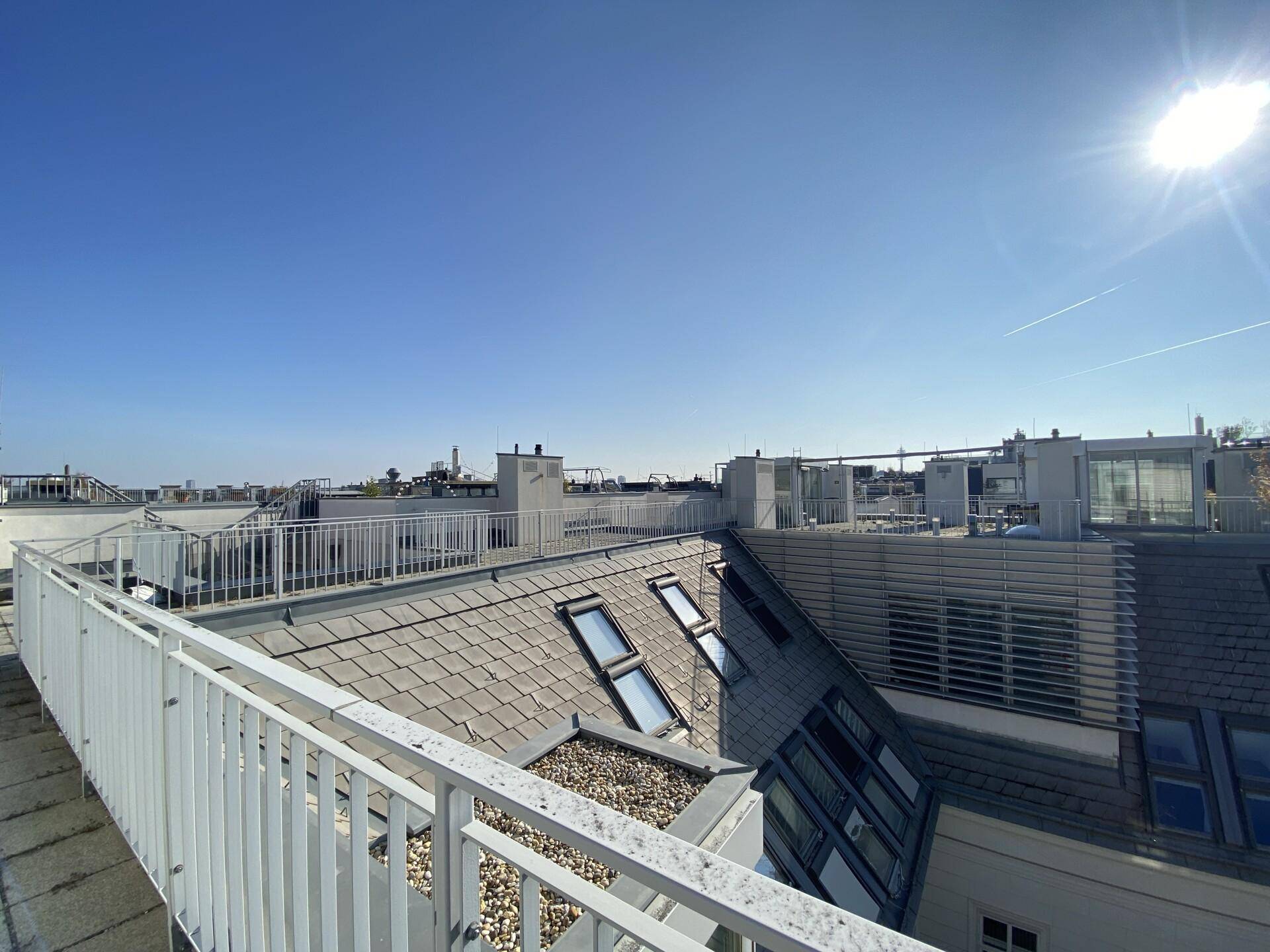 Sonniger Dachterrassenbereich mit weitem Blick über die umliegenden Dächer und den Himmel.