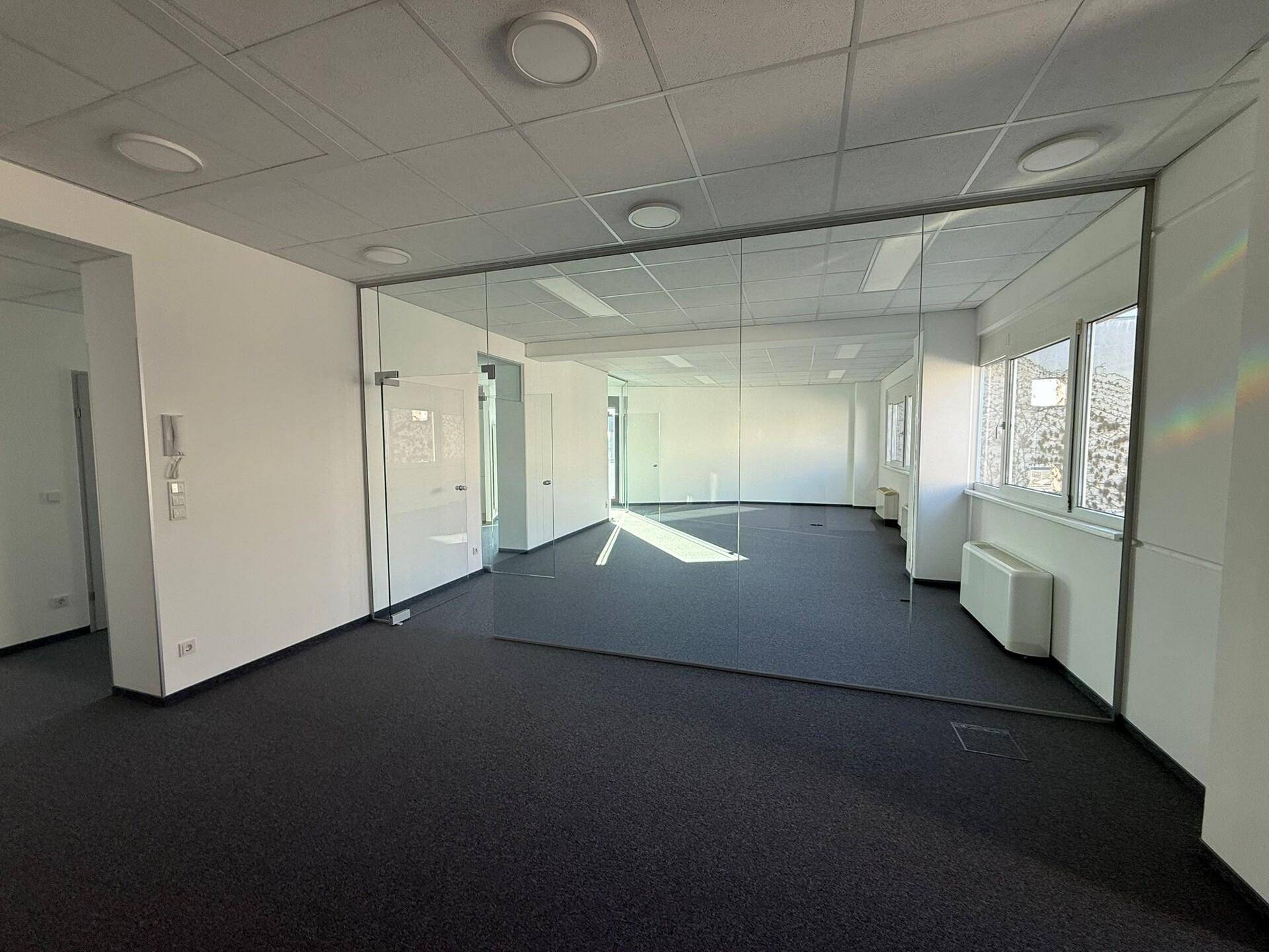 Helles, modernes Büro mit Teppichboden und Glaswänden, das viel Tageslicht erhält und gut gepflegt ist.