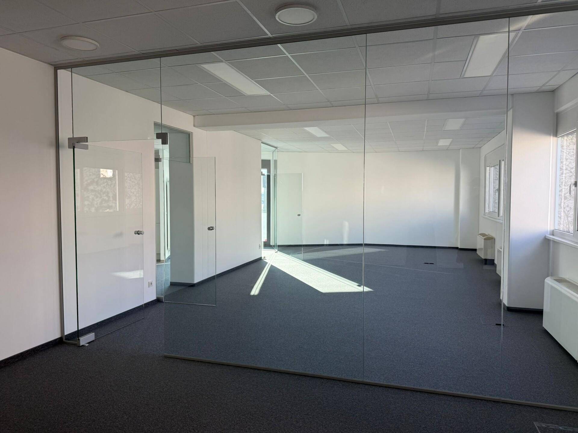 Modernes Büro mit Glaswänden und Teppichboden, das eine helle und offene Arbeitsumgebung bietet und gut gepflegt ist.