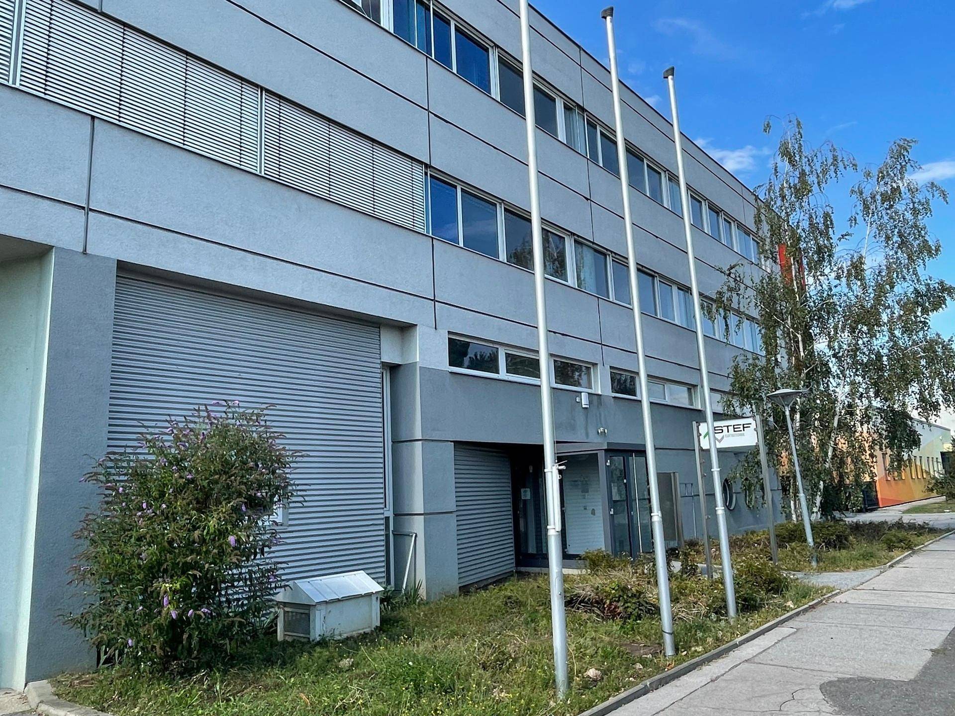 Moderne Fassade eines Bürogebäudes mit großen Fenstern und Rollläden an einem sonnigen Tag, gut gepflegt.