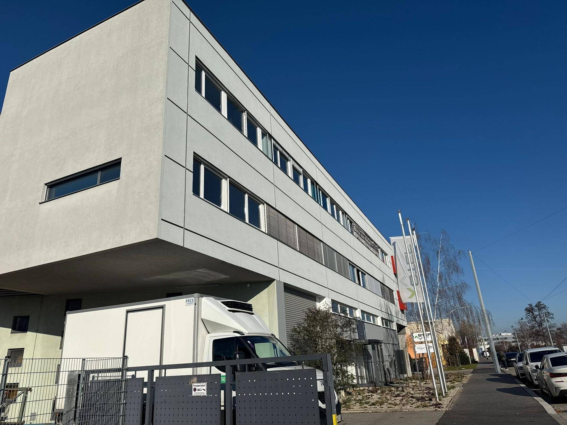 Ansicht eines modernen Bürogebäudes mit weißer Fassade und großen Fenstern an einem sonnigen Tag.