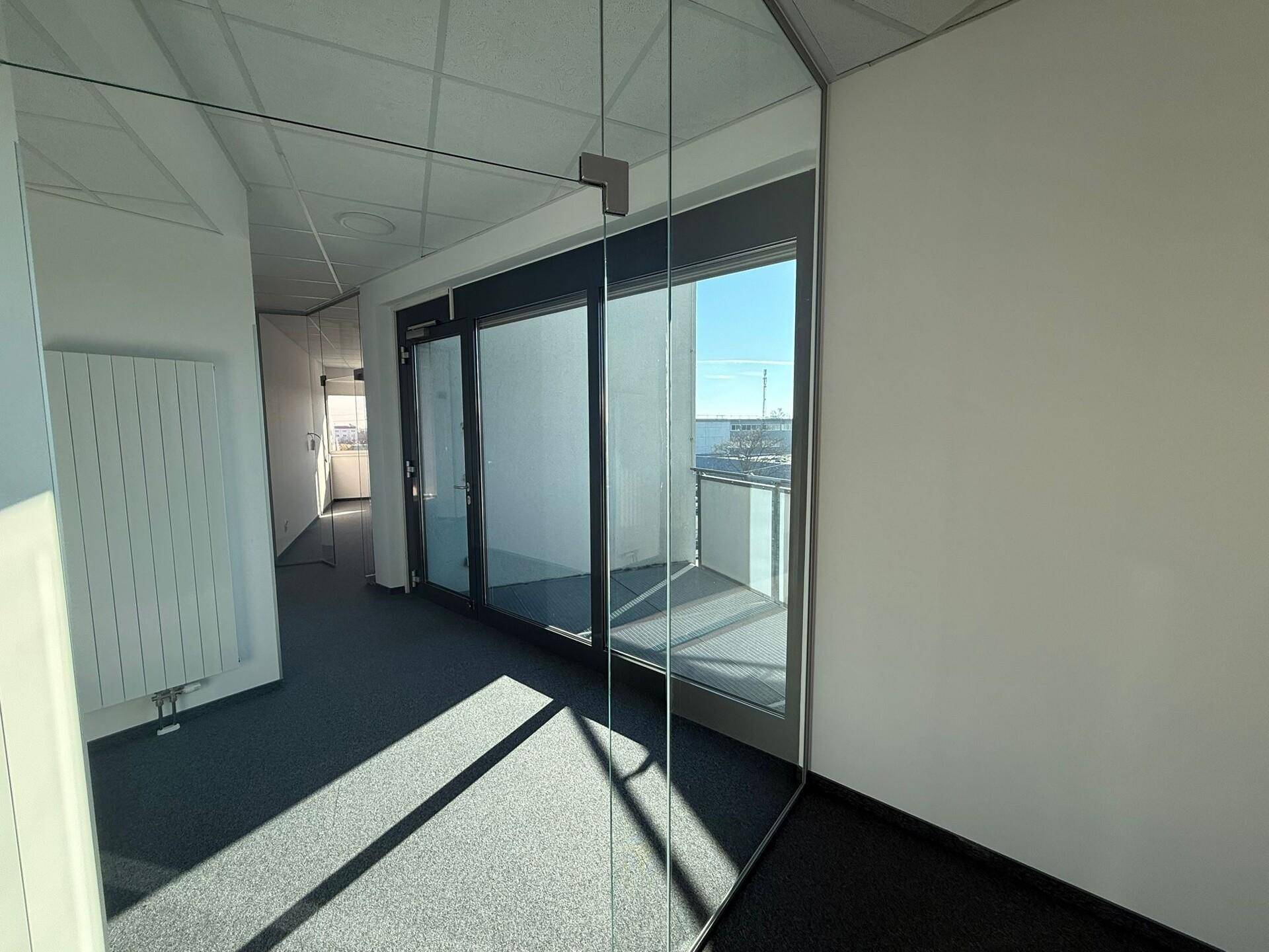 Büroraum mit Glaswänden und Zugang zu einem Balkon, der viel natürliches Licht hereinlässt und modern ist.