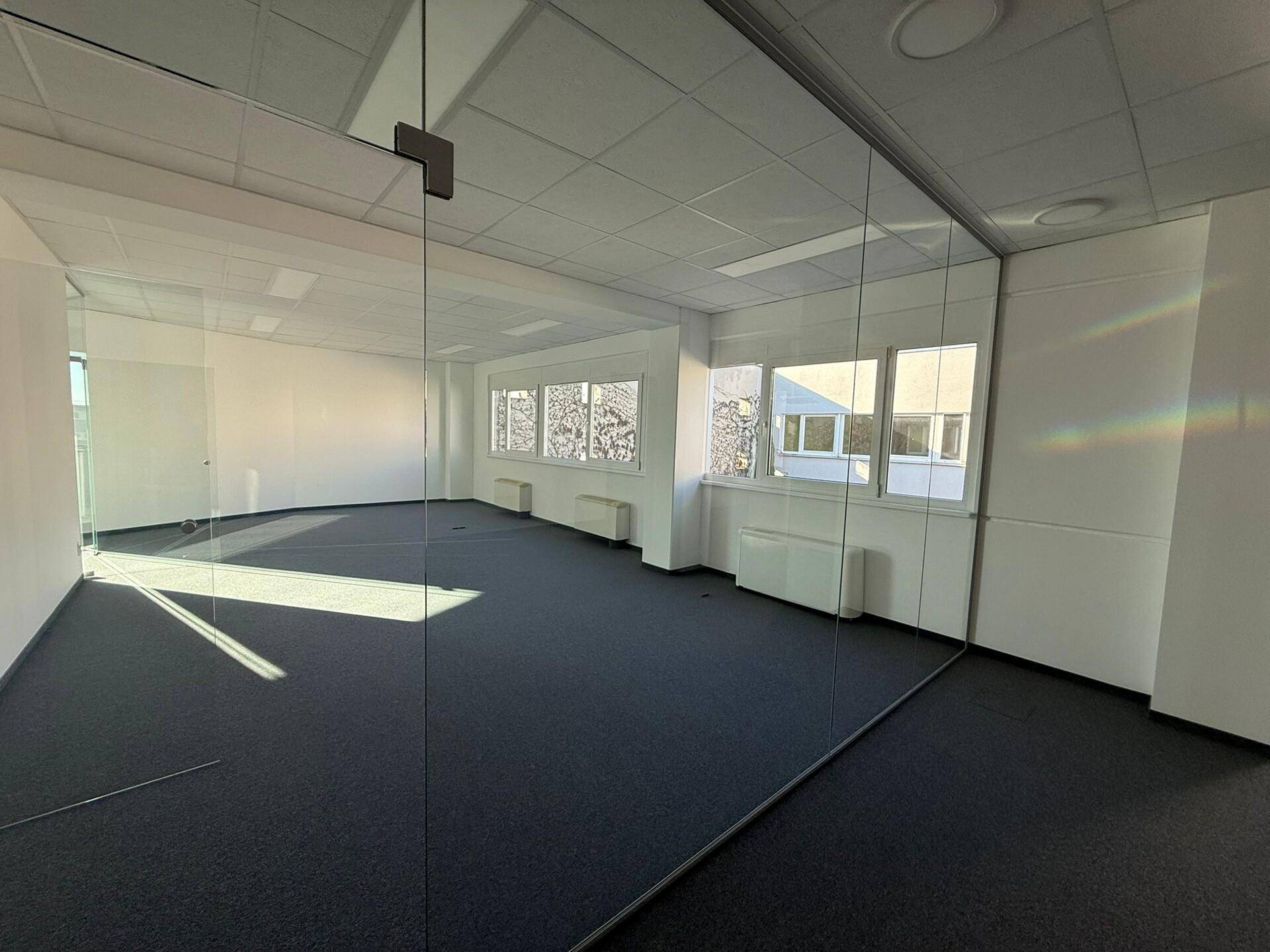 Modernes Büro mit Glaswänden und Teppichboden, das eine helle und offene Arbeitsumgebung bietet und gut gepflegt ist.