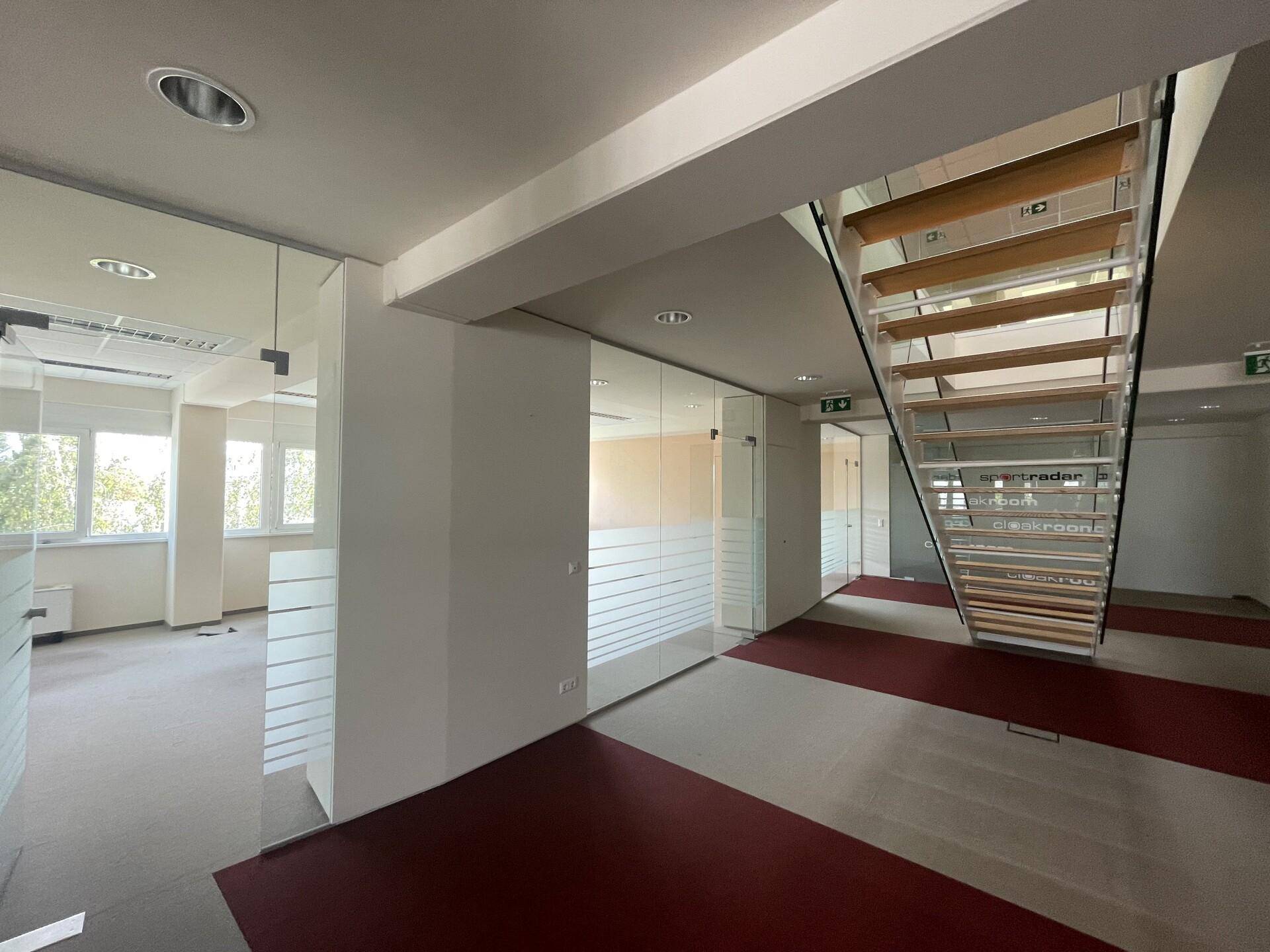 Moderner Bürobereich mit offener Holztreppe, Glaswänden und Teppichboden in verschiedenen Farben, sehr ansprechend.