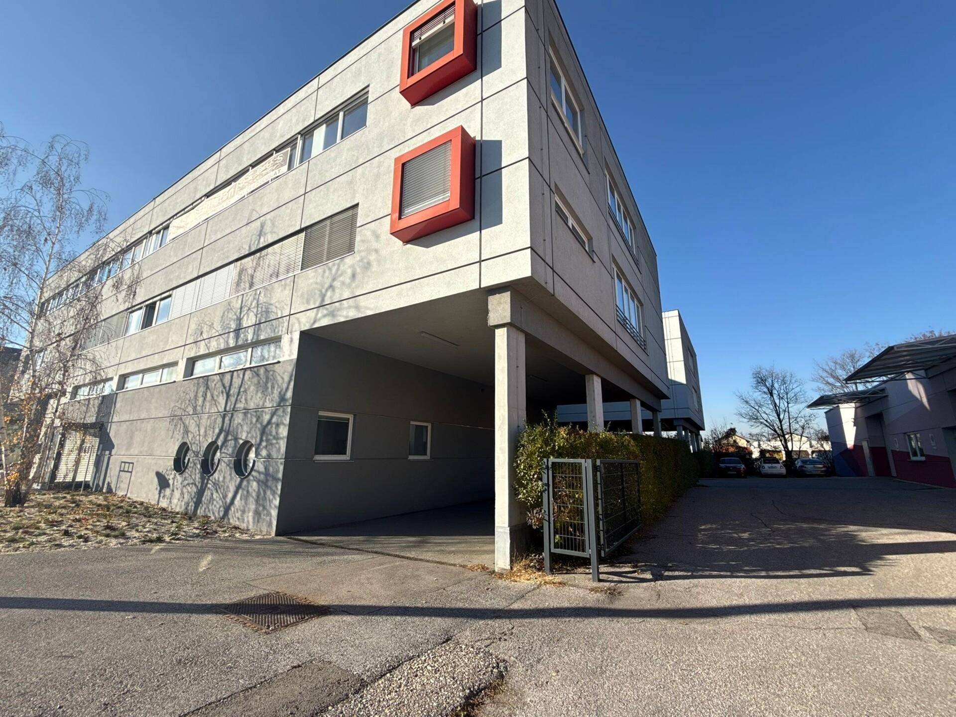 Ansicht eines modernen Bürogebäudes mit roten Akzenten und überdachtem Eingangsbereich.