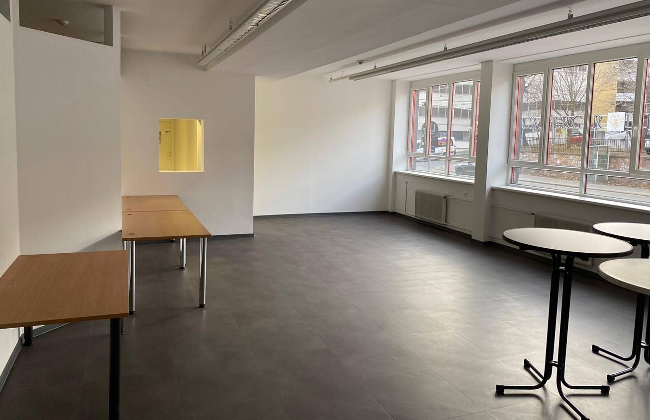 Großer, leerer Raum mit dunklem Boden, weißen Wänden und vielen Fenstern, ideal für Büronutzung.