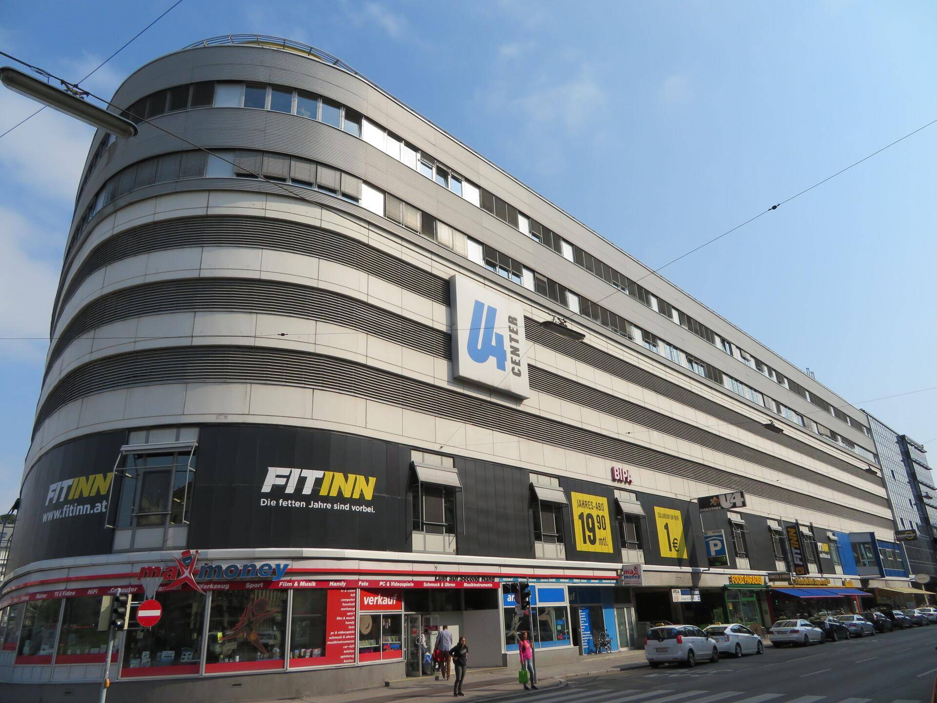 Ein großes, modernes Geschäftsgebäude mit abgerundeter Fassade und verschiedenen Ladenfronten im Erdgeschoss.