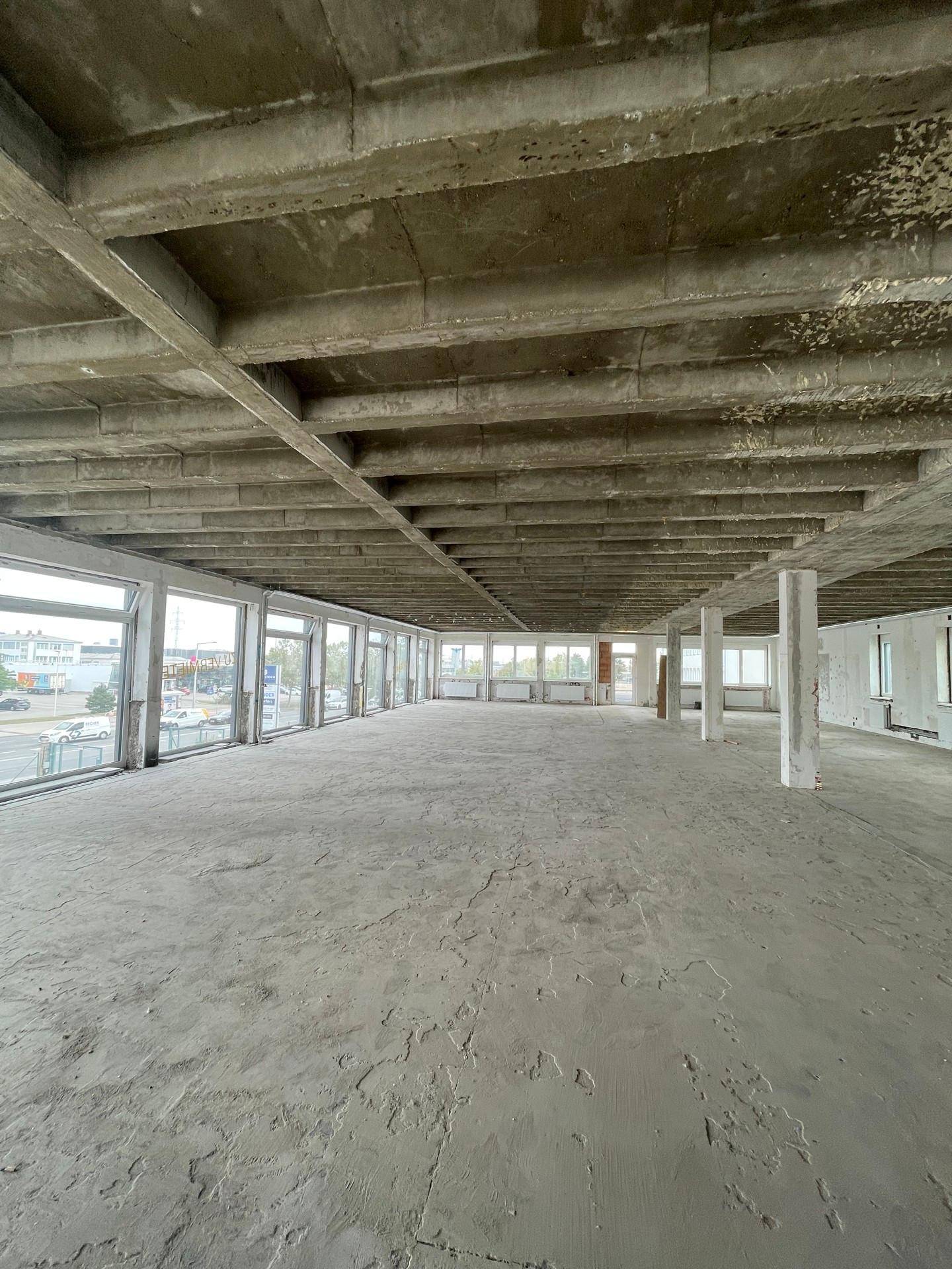Großer, leerer Gewerberaum mit Sichtbetondecke, Betonboden und weiten Fensterfronten, bereit für den Ausbau.