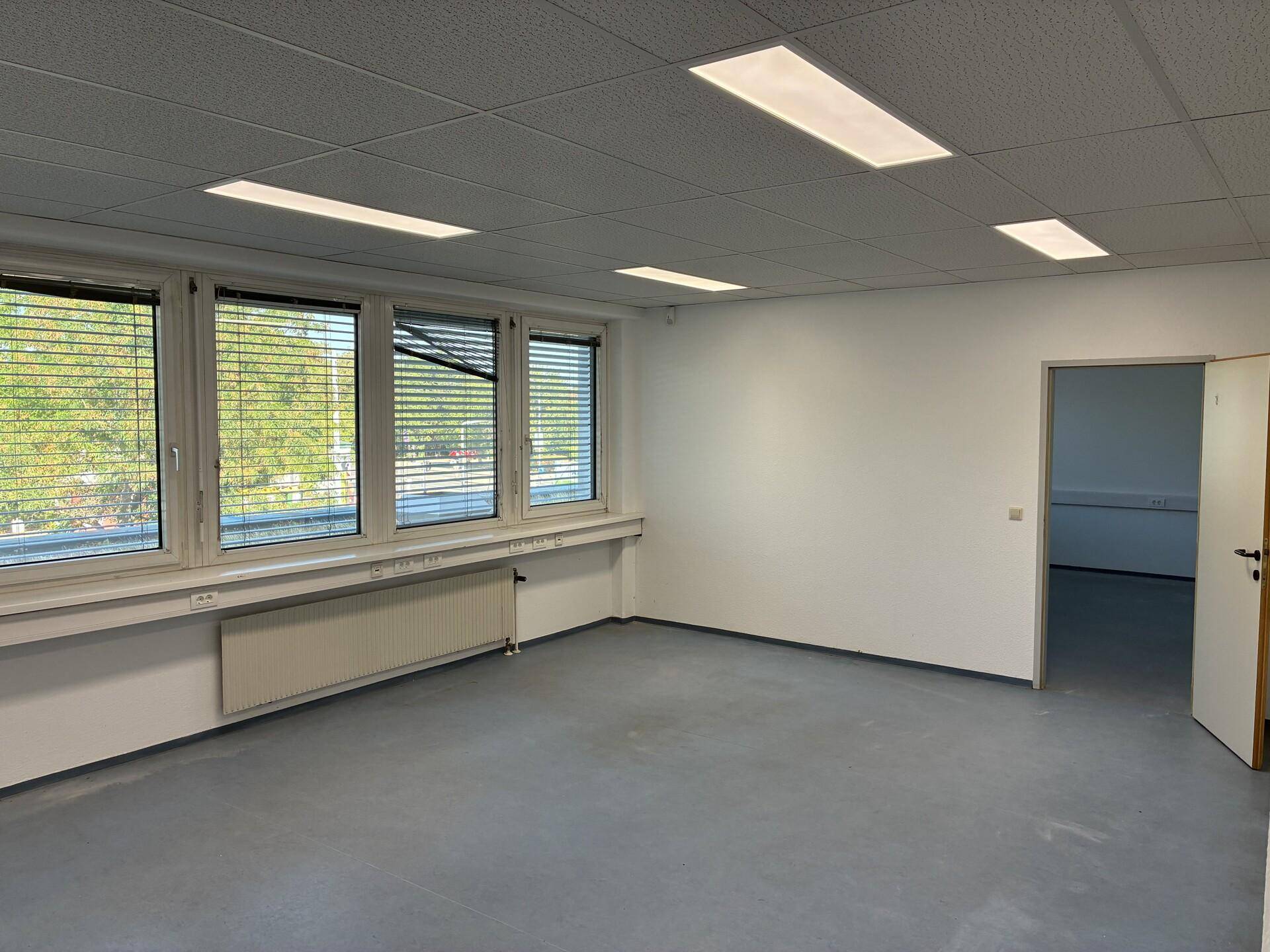 Heller, leerer Büroraum mit großen Fenstern, Jalousien und einem funktionalen Deckenbeleuchtungssystem.