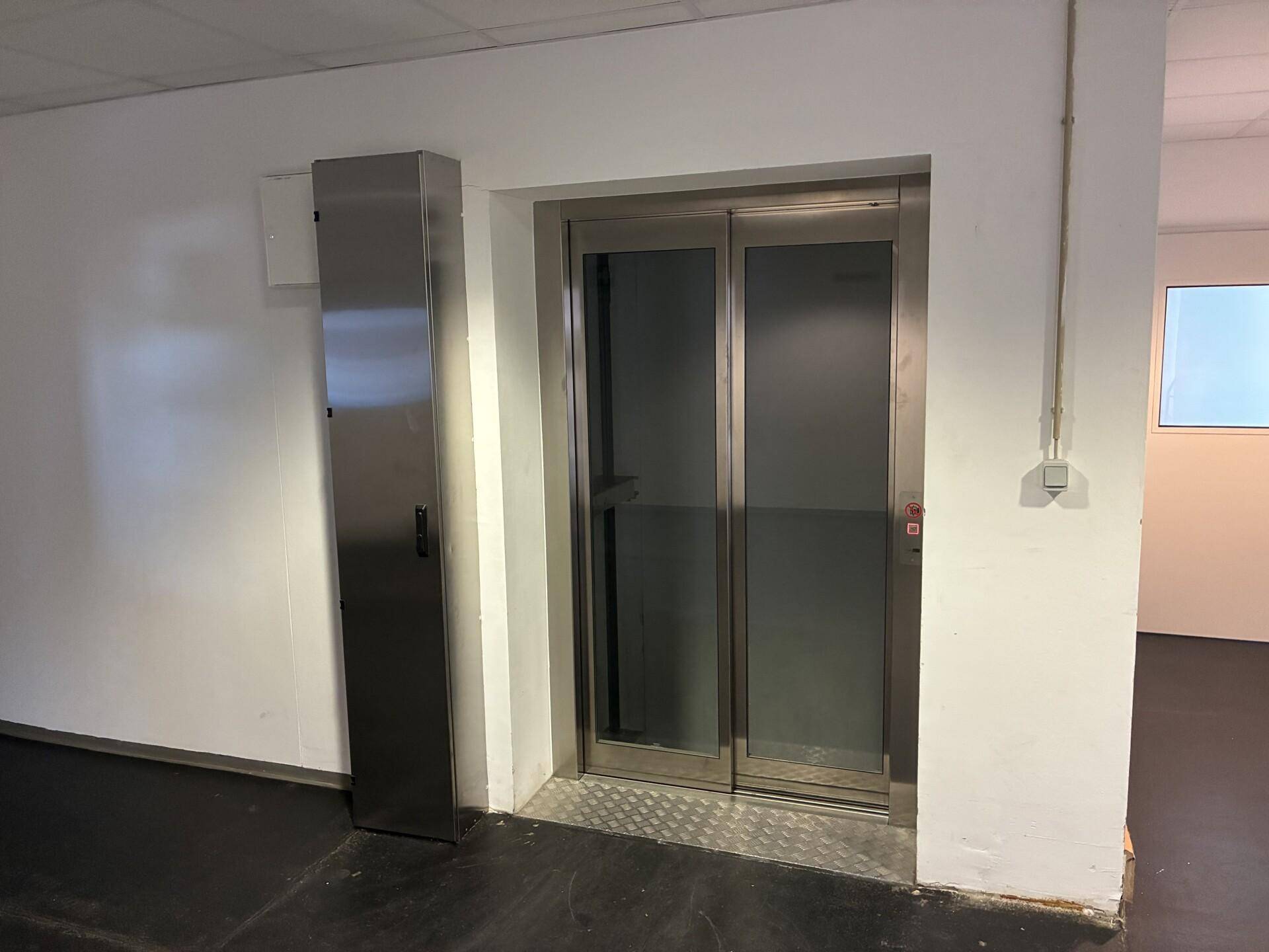 Moderner Aufzug mit Edelstahltüren und Glaspaneelen in einem Gebäude, bereit zur Nutzung.
