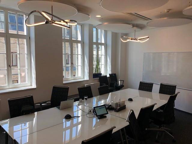 Heller Konferenzraum mit großem weißen Tisch, modernen Leuchten und Blick auf die Stadt.