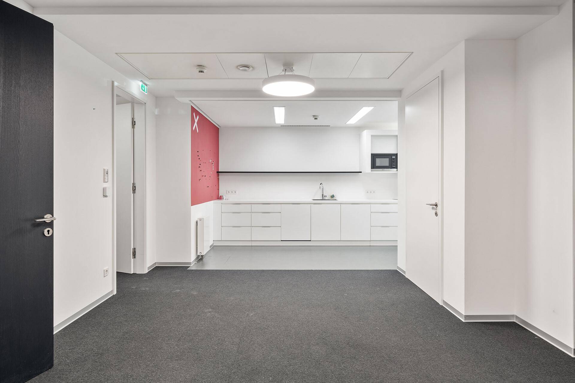 Moderne Teeküche mit weißen Schränken, Mikrowelle und roter Akzentwand.