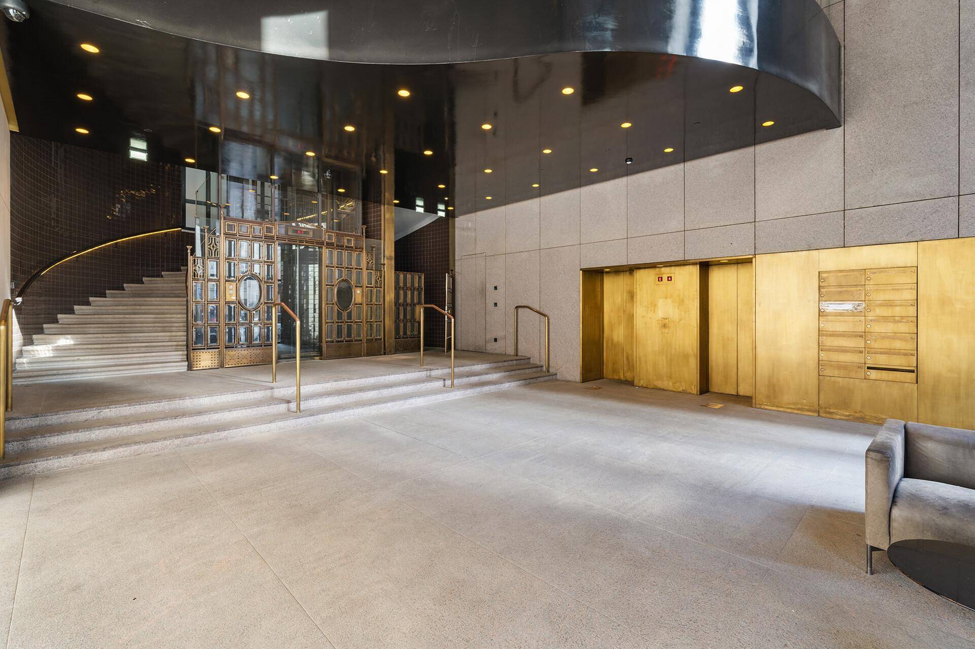 Elegante Lobby mit goldfarbenen Aufzügen, breiter Treppe und modernem Design.