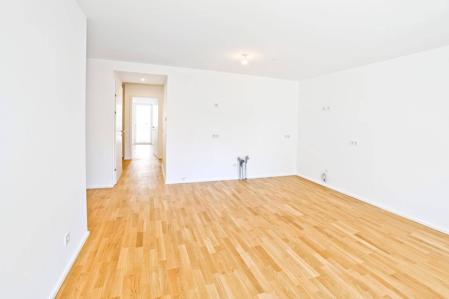 Geräumiges, helles Zimmer mit Parkettboden und weiß gestrichenen Wänden, mit Blick in den Flur.
