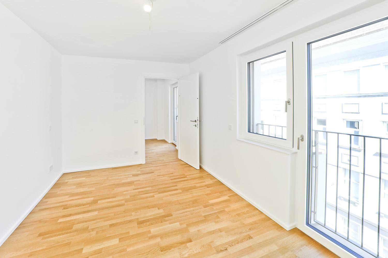 Leeres Zimmer mit Parkettboden und Zugang zu einem französischen Balkon, bietet viel Tageslicht.