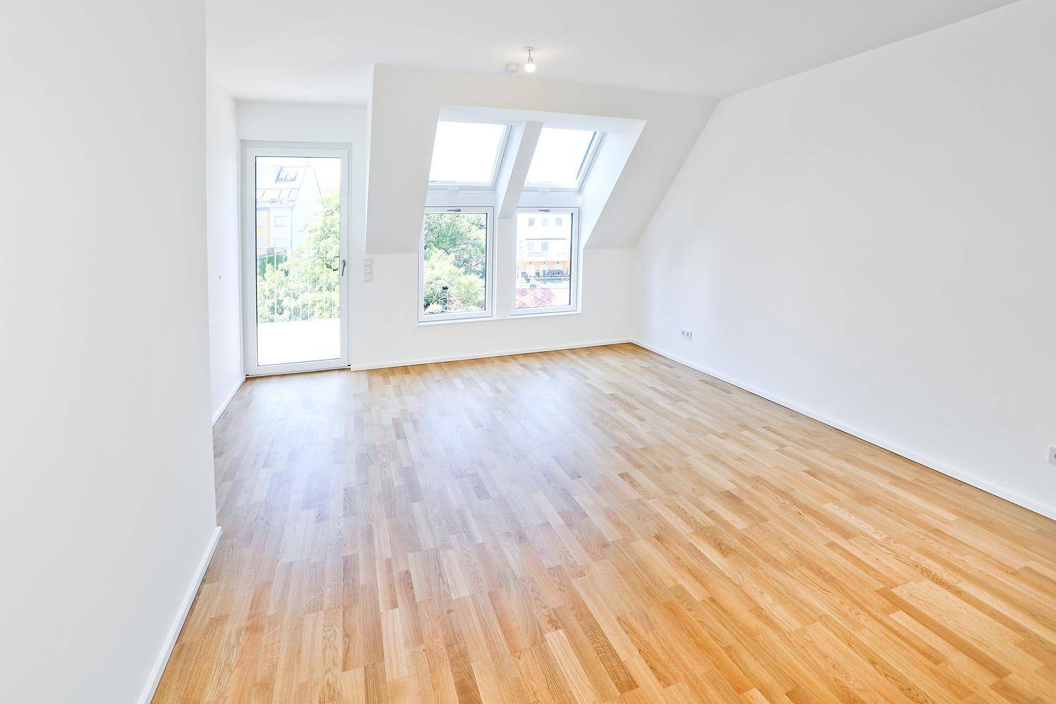 Lichtdurchfluteter Wohnbereich mit Holzboden und Zugang zu einem Außenbereich durch eine Glastür.