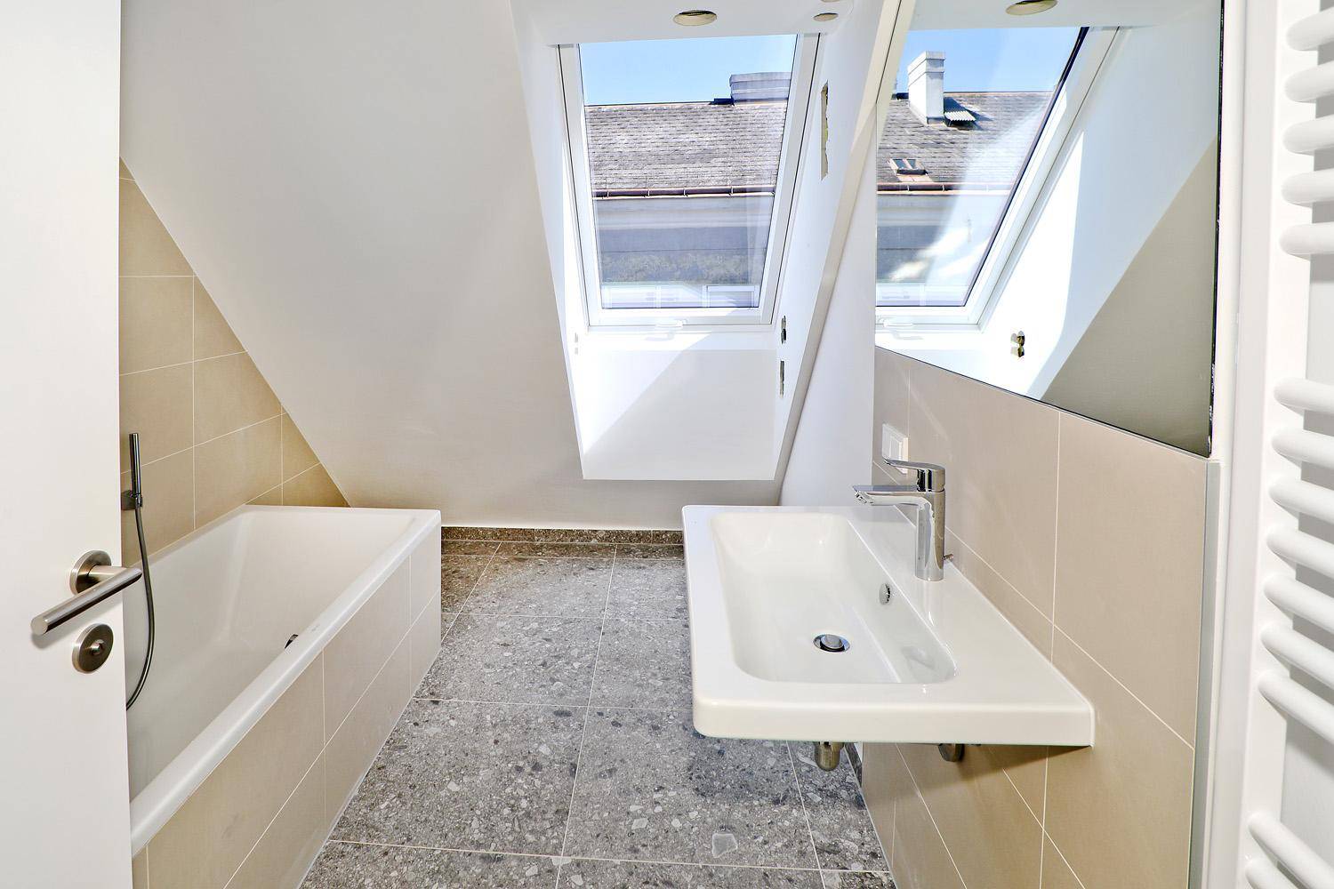 Modernes Badezimmer mit Badewanne, Waschbecken und Dachfenstern unter einer Dachschräge.