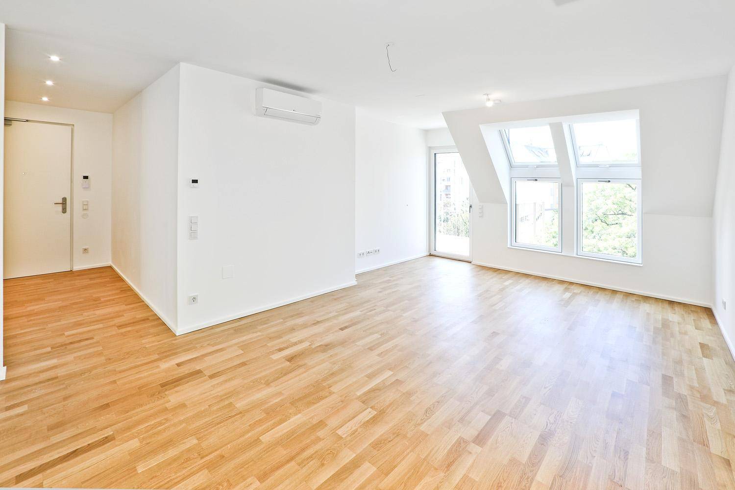 Heller Wohnraum mit Parkettboden, Klimaanlage und großen Dachfenstern im Dachgeschoss.