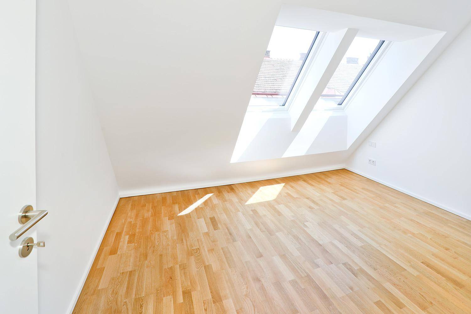 Helles Schlafzimmer mit Parkettboden und schrägen Wänden unter großen Dachfenstern.
