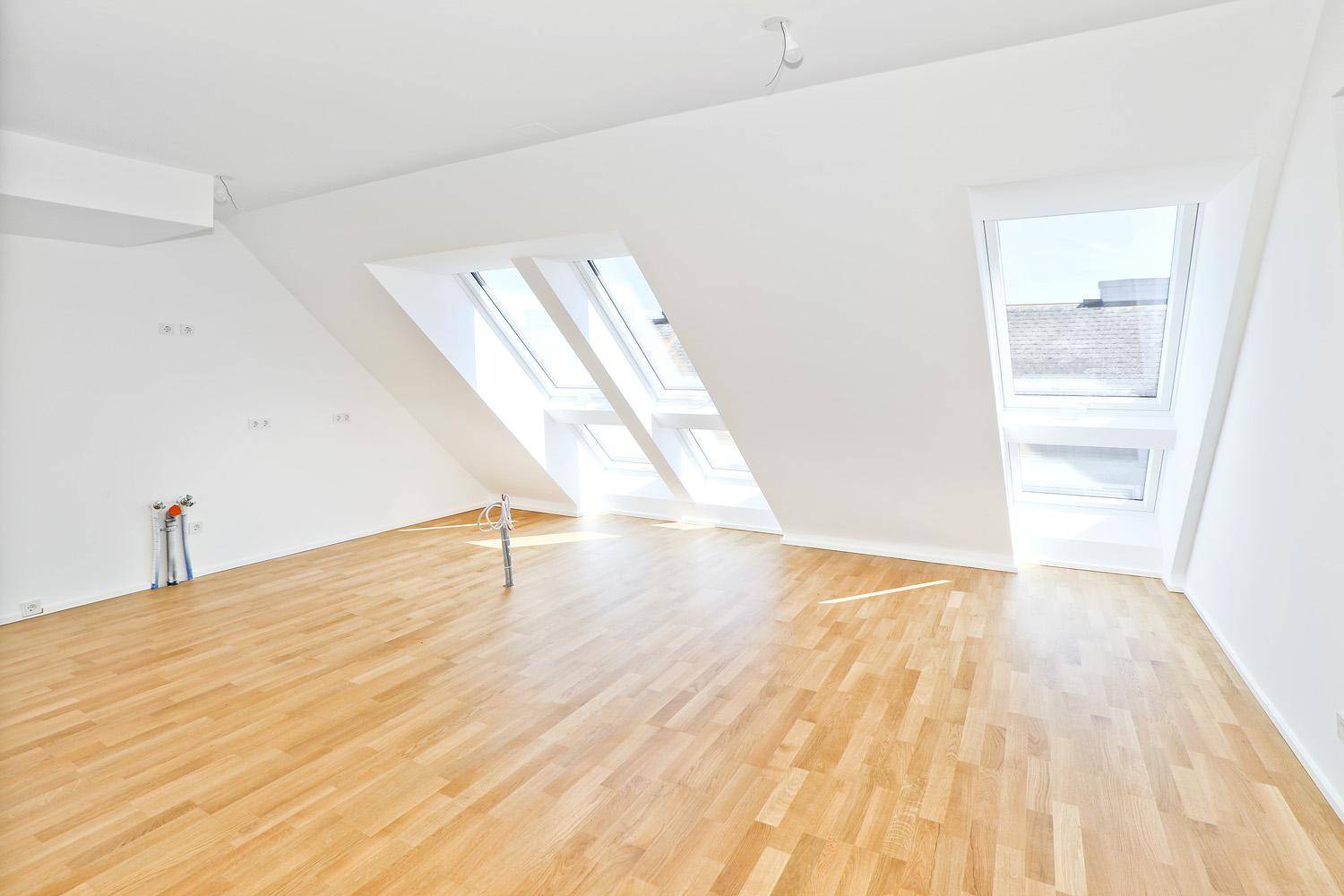 Lichtdurchflutetes Zimmer im Dachgeschoss mit Parkettboden und mehreren Dachfenstern.