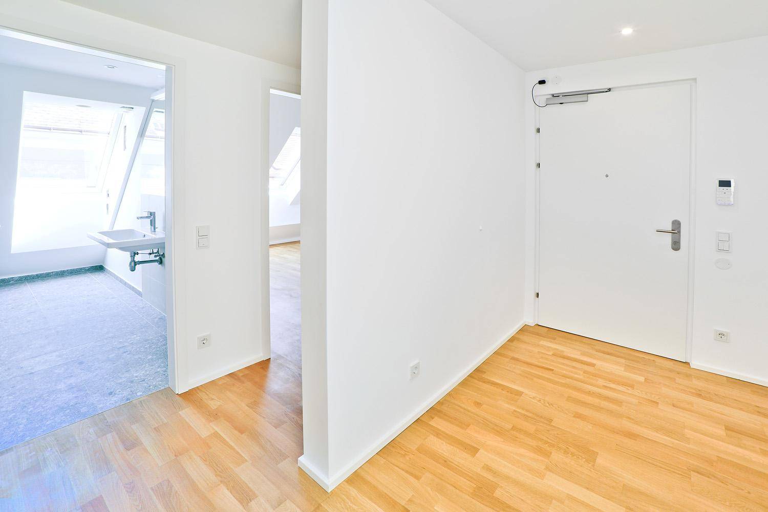 Eingangsbereich mit Holzboden und Blick in ein modernes Badezimmer mit Dachfenstern.