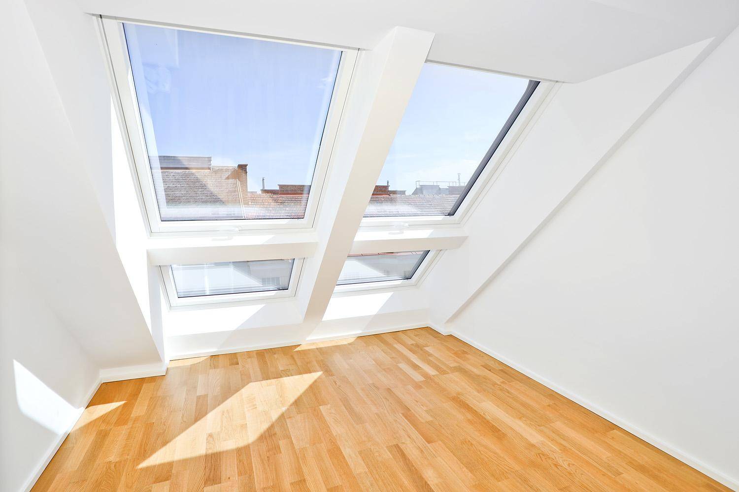 Helles Dachzimmer mit Parkettboden und großen Dachfenstern, die viel Sonnenlicht hereinlassen.