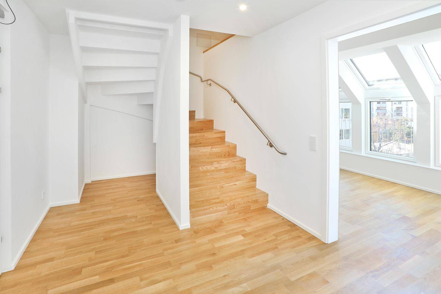 Heller Eingangsbereich mit Holztreppe und Parkettboden, der zu weiteren Räumen führt.