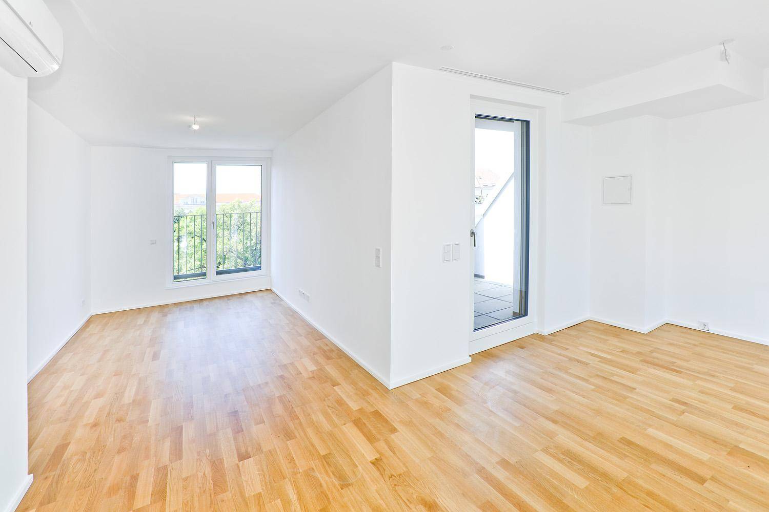Geräumiges Wohnzimmer mit Parkettboden, Klimaanlage und Zugang zu einem Außenbereich.