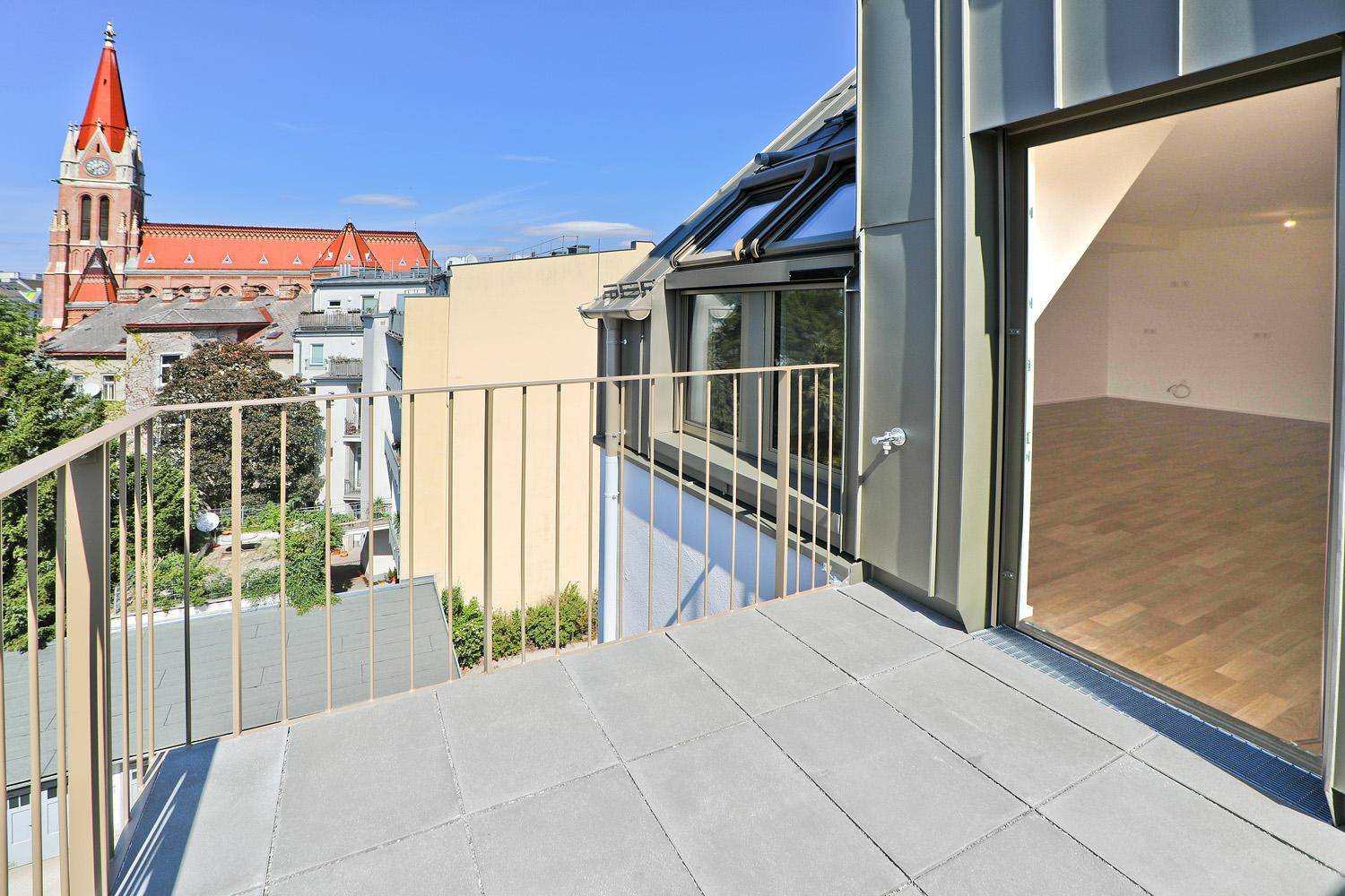 Balkon mit Metallgeländer und Blick auf die Stadt, angrenzend an einen hellen Innenraum.