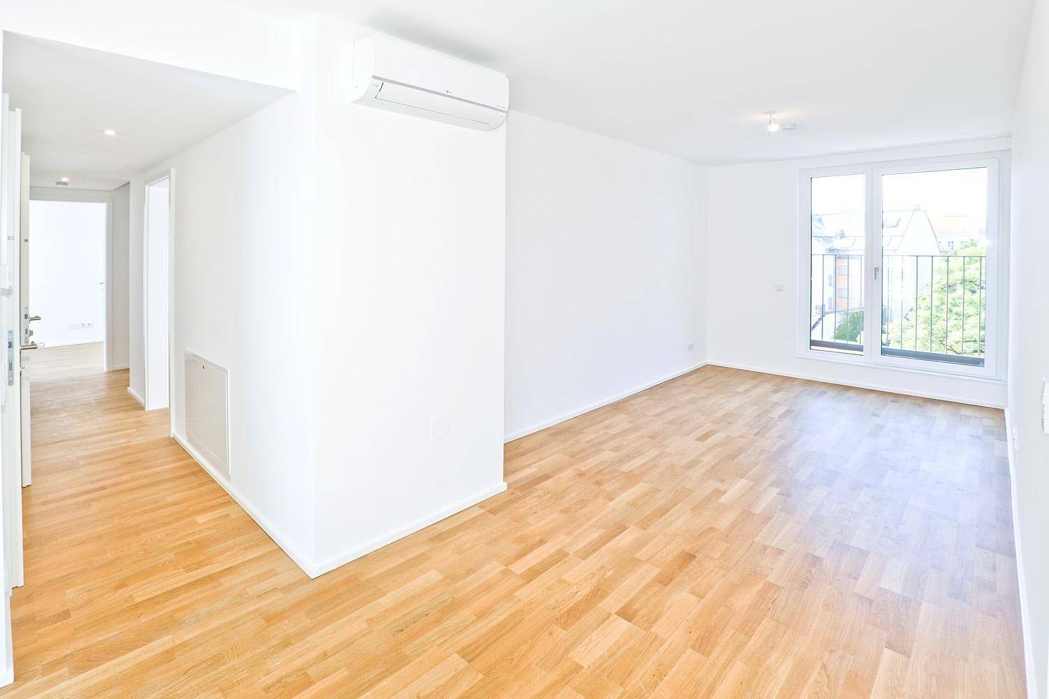 Helles Wohnzimmer mit Parkettboden, Klimaanlage und Fenster mit Blick ins Grüne.