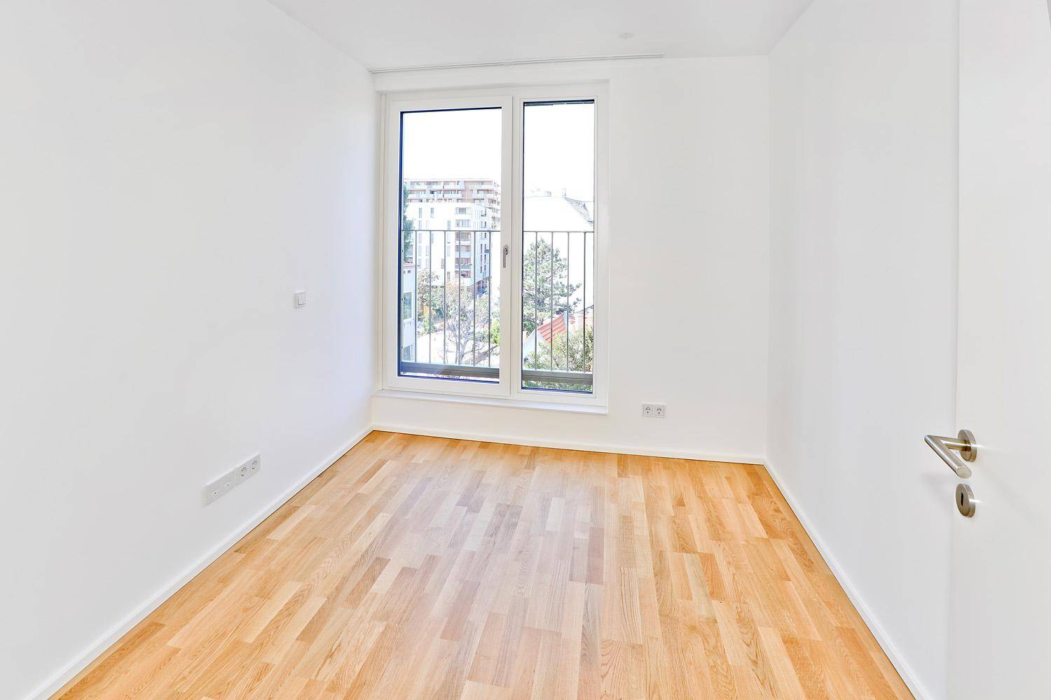 Helles Schlafzimmer mit Parkettboden, weißen Wänden und einem Fenster mit französischem Balkon.