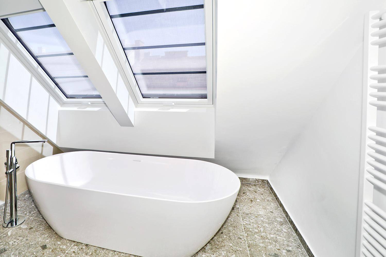 Modernes Badezimmer mit freistehender Badewanne, Fliesenboden und großem Dachfenster.
