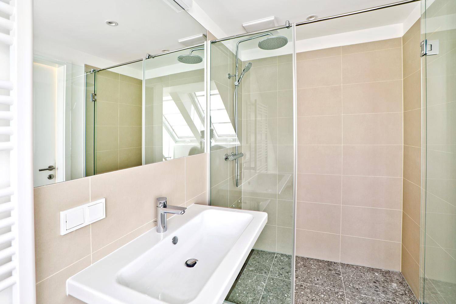 Modernes Badezimmer mit Einzelwaschbecken, großem Spiegel und begehbarer Dusche mit Regenduschkopf.