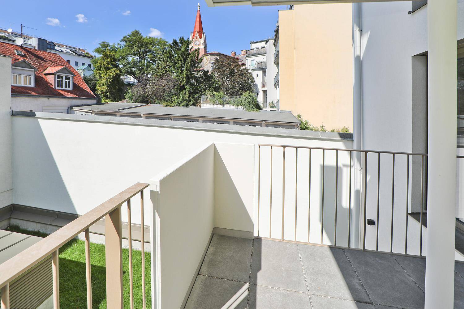 Geräumiger Balkon mit Fliesenboden und seitlichem Blick auf die Stadt und einen Kirchturm.